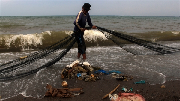 Một ngư dân ở Indonesia tìm kiếm lưới đánh bắt của mình trên một bãi biển đầy rác thải nhựa. Các thiết bị đánh bắt bị bỏ đi đã trở thành mối đe dọa nghiêm trọng đối với môi trường. Nguồn ảnh: Nikkei Asian Review.
