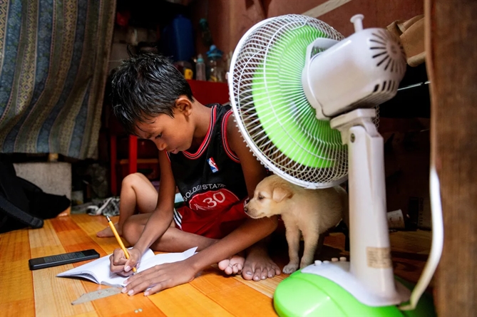 Một học sinh làm bài ở nhà trước quạt sau khi các lớp học trực tiếp tạm dừng vì nắng nóng ở Manila, Philippines