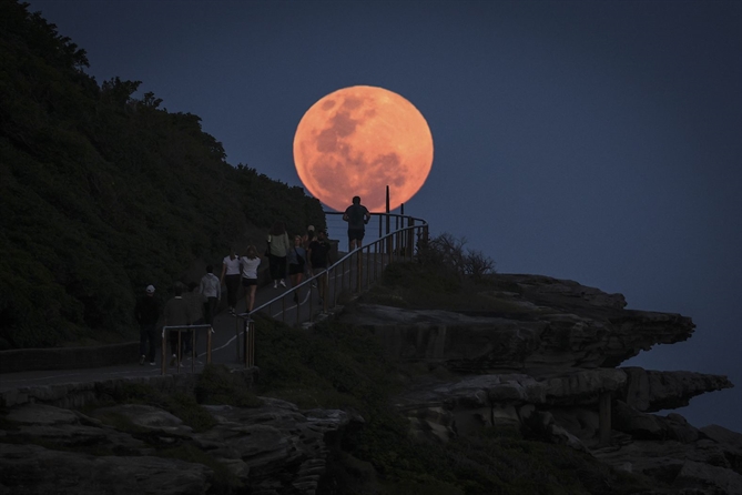 Mặt trăng mọc phía sau những người đi bộ gần bãi biển Bondi của Sydney vào thứ năm. David Gray/AFP/Hình ảnh Getty